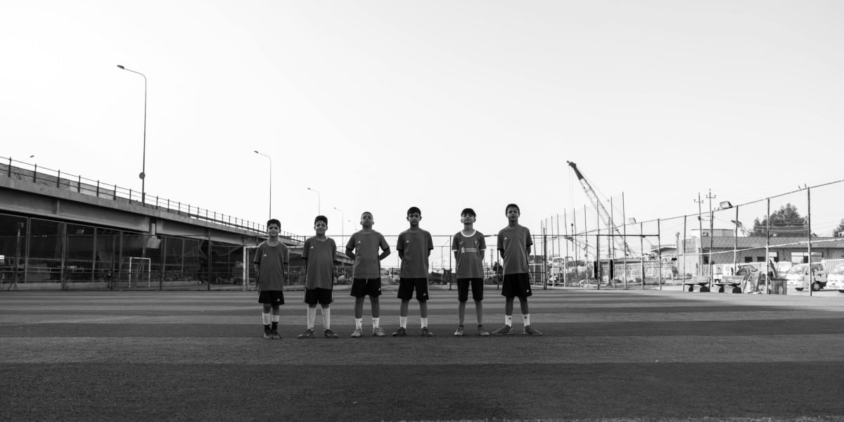 Black and white photo of a youth soccer team lined up on a field beneath an overpass.